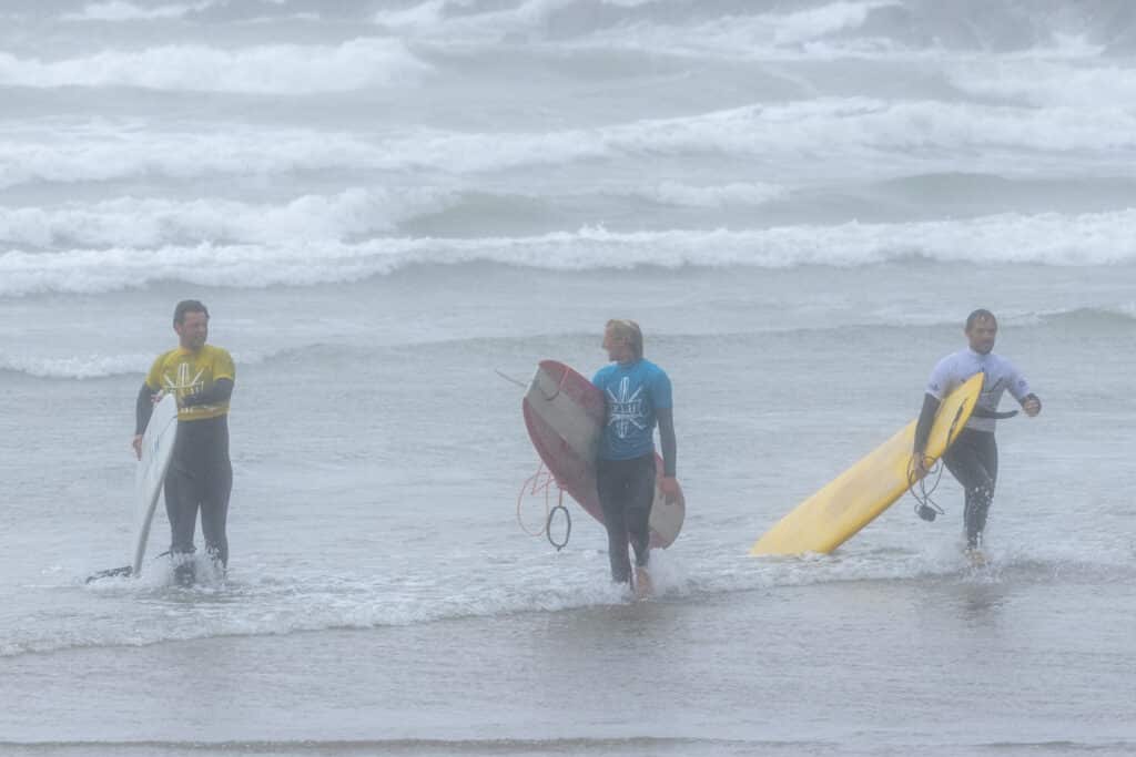 Surfers walk back from the sea in the saunton longboard classic. Windy and grey dull looking day as 3 surrfers walk towards the camera carrying longboards